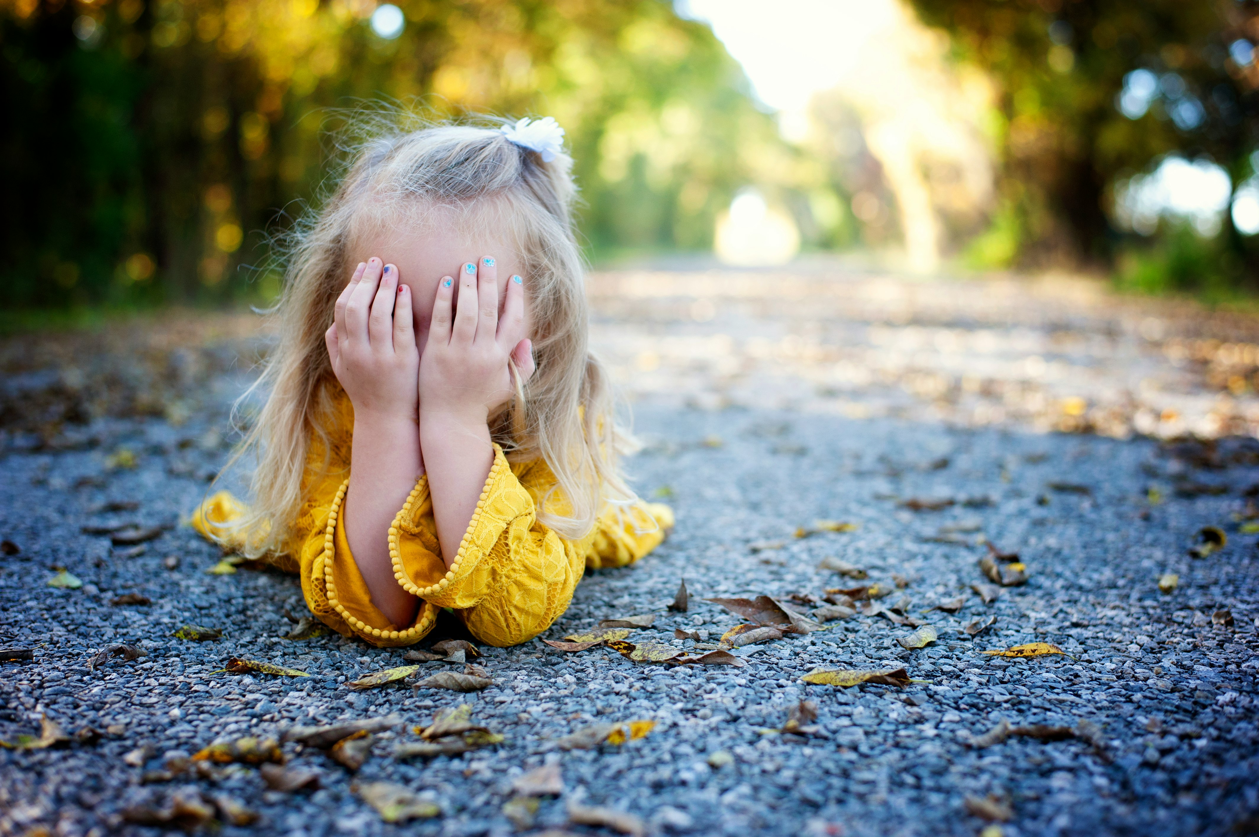 girl in yellow dress sitting on ground with dried leaves during daytime